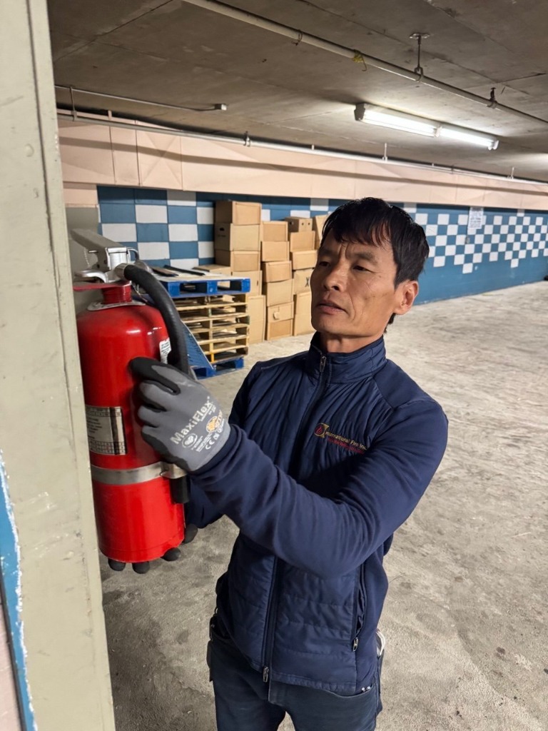 A technician from Fire Safety Industries installing and testing a portable fire extinguisher in a commercial building in Albuquerque
